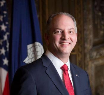 Governor John Bel Edwards standing in from of a flag